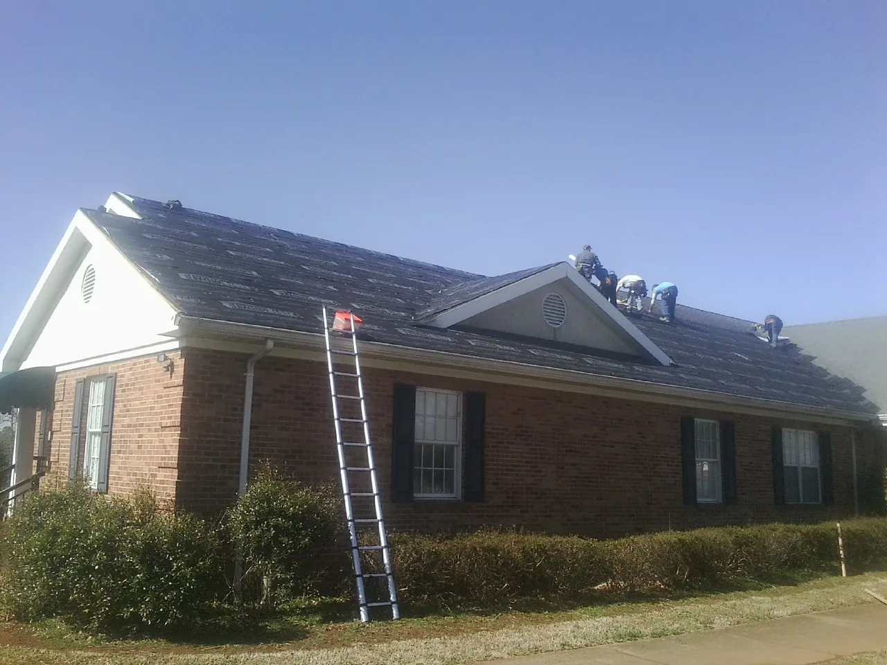 Crew tearing shingles off a brick ranch roof with a ladder set — Metal Roof Repair work by our crew in La Palma