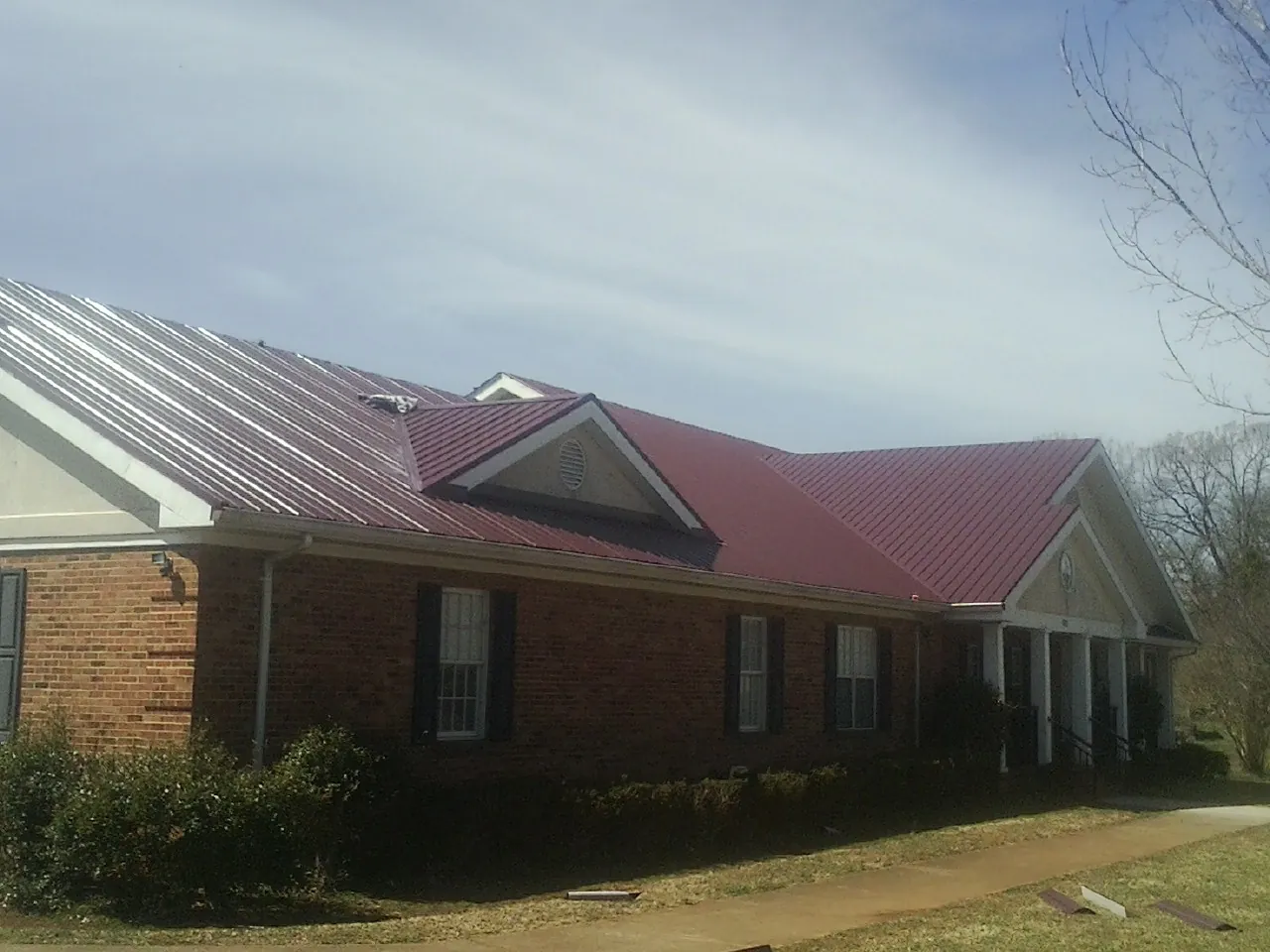 Red metal roof with gabled entries on a long brick building, from a Hail Damage Roof Repair job in La Palma