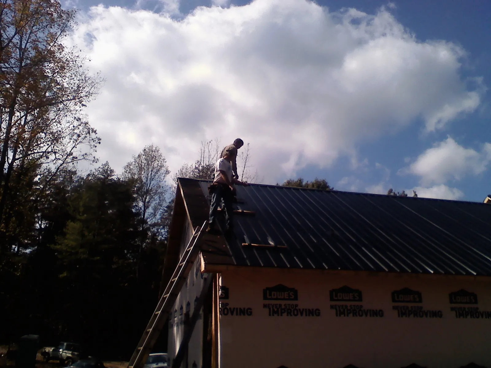 Roofer fastening dark metal panels high against a cloudy sky, from a Roof Inspection job in La Palma